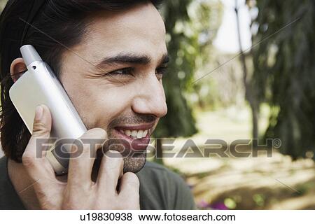 Stock Photo - Close-up of a young man smiling and using a mobile phone. Fotosearch