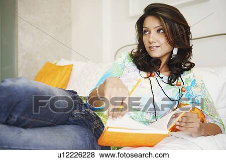 Stock Photo - Close-up of a young woman lying on the bed and holding a book. Fotosearch