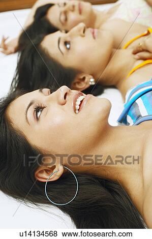 Stock Photo - High angle view of three young women lying on the bed. Fotosearch