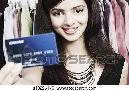 Stock Photo - Portrait of a young woman standing in a clothing store and holding a credit card. Fotosearch