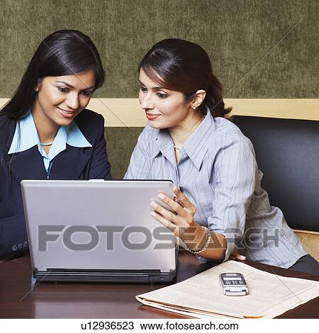 Stock Image - Two businesswomen sitting in an office and using a laptop. Fotosearch