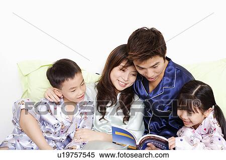Stock Photography - Close-up of a mid adult man and a young woman with their children reading a book on the bed. Fotosearch