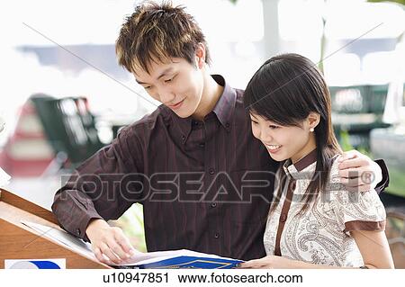 Stock Image - Close-up of a young couple reading a book and smiling. Fotosearch