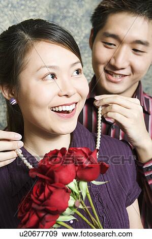 Stock Photo - Close-up of a young man tying a necklace around a young woman's neck. Fotosearch