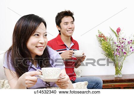 Stock Image - Close-up of a young woman and a mid adult man drinking tea. Fotosearch