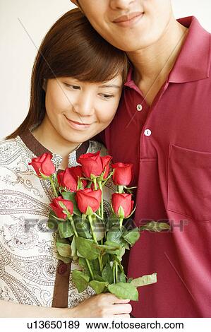 Close-up of a young woman holding a bouquet of red roses and standing with a young man View Large Photo Image Stock Photo - Close-up of a young woman holding a bouquet of red roses and standing with a young man. Fotosearch