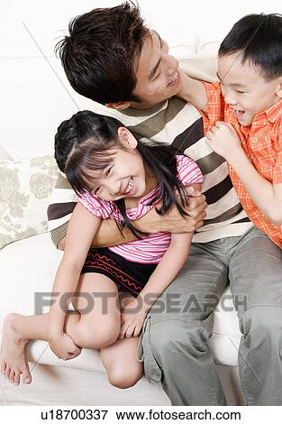 Stock Photo - Mid adult man sitting on a couch with his son and daughter. Fotosearch