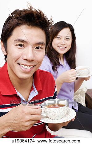 Picture - Portrait of a mid adult man drinking a cup of tea with a young woman sitting behind him. Fotosearch
