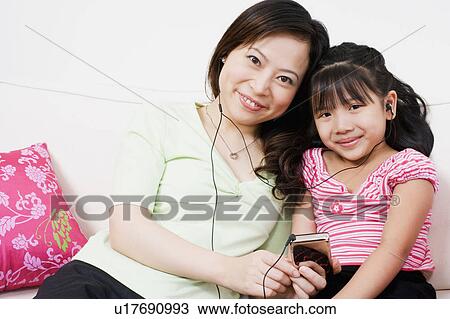 Stock Image - Portrait of a young woman and her daughter listening to an MP3 player. Fotosearch