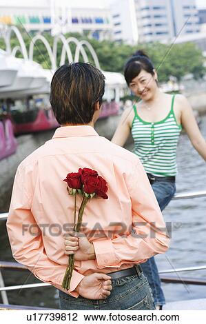 Rear view of a young man holding a bunch of roses behind his back View Large Photo Image Stock Image - Rear view of a young man holding a bunch of roses behind his back. Fotosearch