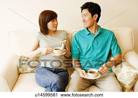 Stock Image - Young couple sitting on a couch and looking at each other. Fotosearch