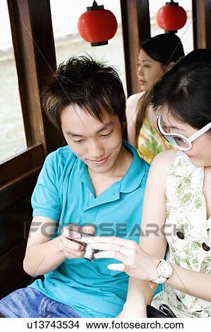 Picture - Close-up of a young couple looking at a digital camera with a young woman behind them. Fotosearch
