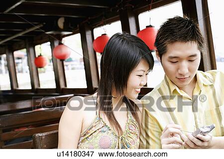 Stock Photo - Close-up of a young man using a mobile phone beside a young woman. Fotosearch