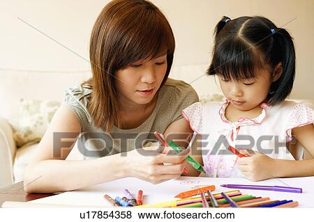 Stock Photo - Close-up of a young woman teaching her daughter to color. Fotosearch