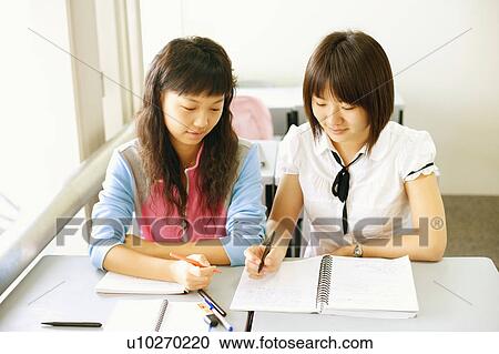 High angle view of two young women holding pens and looking at a spiral notepad View Large Photo Image Stock Image - High angle view of two young women holding pens and looking at a spiral notepad. Fotosearch