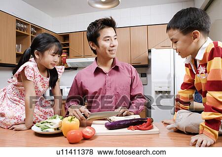Stock Photo - Mid adult man and his children cutting vegetables at a kitchen counter. Fotosearch