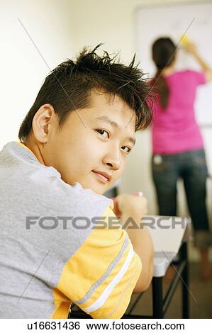 Rear view of a young man sitting in a classroom View Large Photo Image Stock Photograph - Rear view of a young man sitting in a classroom. Fotosearch