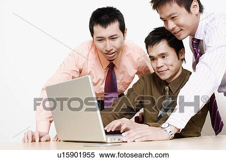 Stock Photography - Three businessmen using a laptop and smiling. Fotosearch