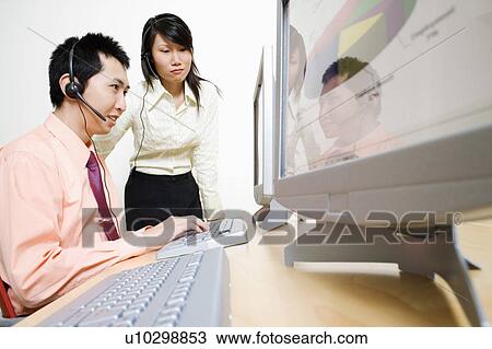 Stock Image - Two customer service representatives working on a computer. Fotosearch