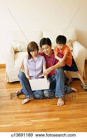 Stock Photo - Young couple shopping online with a credit card and their son beside them. Fotosearch