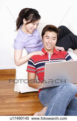 Stock Photography - Young woman sitting on a couch with a mid adult man using a laptop. Fotosearch