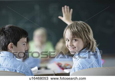 Stock Image - School boy raising hand in class. Fotosearch