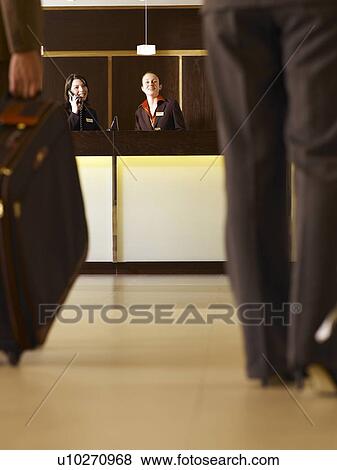 Stock Photo - Businessman and woman approaching hotel reception, low section. Fotosearch
