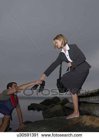 Stock Image - Businesswoman on a dock passing man her shoes. Fotosearch