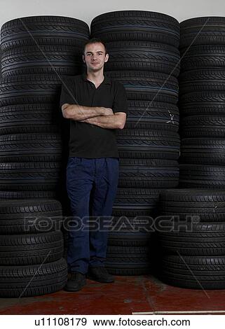 Stock Photo - Mechanic standing by stacks of tires. Fotosearch