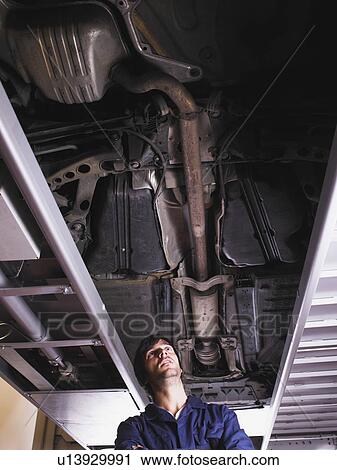 Stock Image - Mechanic standing under raised car. Fotosearch