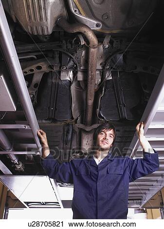 Mechanic standing under raised car View Large Photo Image Stock Image - Mechanic standing under raised car. Fotosearch