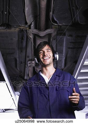 Mechanic standing under raised car listening to music View Large Photo Image Stock Photo - Mechanic standing under raised car listening to music. Fotosearch