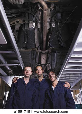 Stock Image - Three mechanics standing under a raised car. Fotosearch