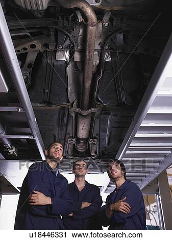 Stock Image - Three mechanics standing under a raised car. Fotosearch