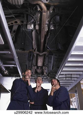 Three mechanics standing under a raised car View Large Photo Image Stock Image - Three mechanics standing under a raised car. Fotosearch