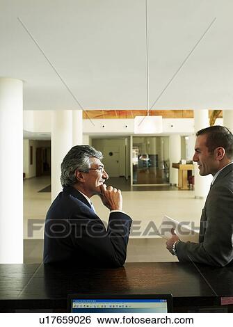 Two businessmen standing in foyer, talking View Large Photo Image Stock Photograph - Two businessmen standing in foyer, talking. Fotosearch