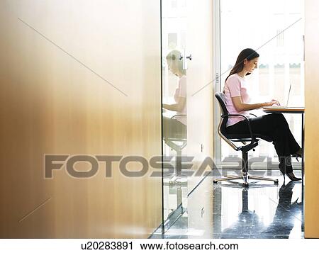 Young businesswoman sitting in office using laptop, side view View Large Photo Image Stock Image - Young businesswoman sitting in office using laptop, side view. Fotosearch