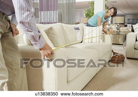 Stock Image - A couple measuring a sofa in a shop.. Fotosearch
