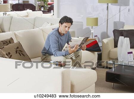 Stock Image - Man sitting on sofa in furniture store.. Fotosearch