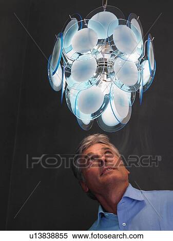 Stock Photography - Mature man standing under illuminated chandelier. Fotosearch