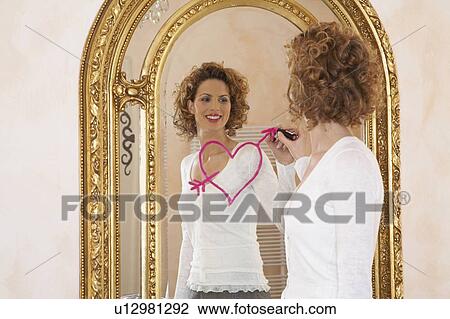 Stock Image - woman drawing heart on mirror with lipstick. Fotosearch