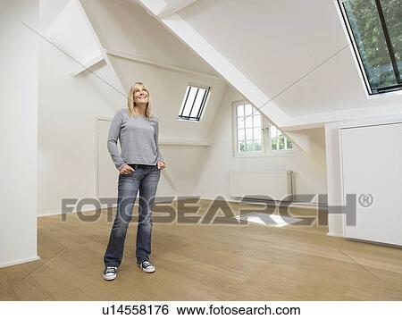 Stock Photograph - Woman standing and looking up inside empty white loft.. Fotosearch