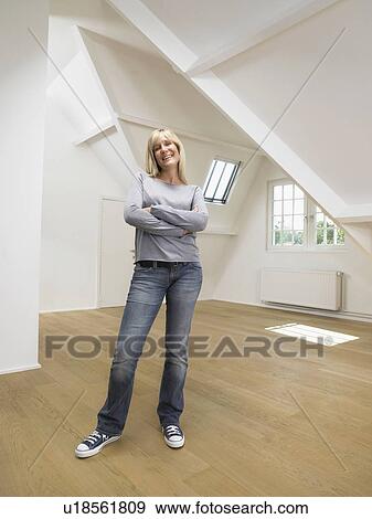 Stock Photo - Woman standing with arms crossed in an empty loft.. Fotosearch