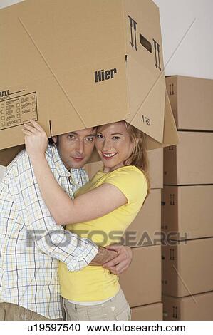 Young couple embracing under cardboard box, smiling, portrait View Large Photo Image Stock Image - Young couple embracing under cardboard box, smiling, portrait. Fotosearch