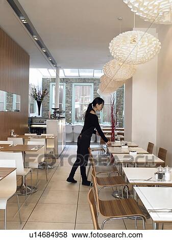 Stock Photo - Young waitress setting tables in empty restaurant. Fotosearch
