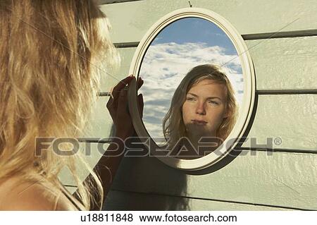 Stock Photo - Young Woman Looking in Mirror outside.. Fotosearch