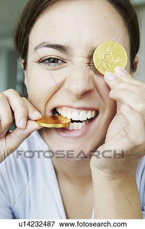 Stock Photo - Amusing woman bites into gold coins. Fotosearch