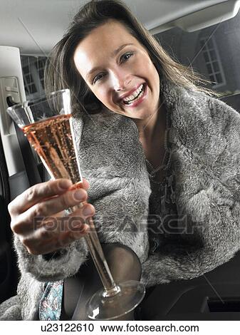 Stock Image - Woman in car, drinking and celebrating. Fotosearch