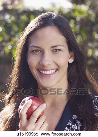 Stock Photography - Young woman smiling and holding apple. Fotosearch