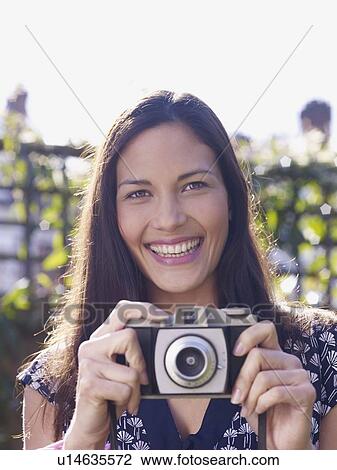 Stock Image - Young woman smiling and holding camera. Fotosearch